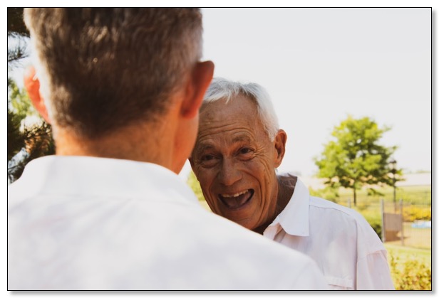 Picture of an older man outdoors laughing looking at younger man, communicating the need for dementia training to have healthy relationships. 